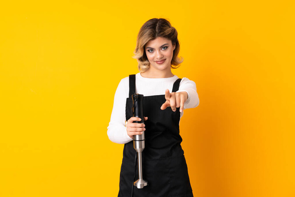 Girl using hand blender isolated on yellow background pointing front with happy expression - Photo, Image