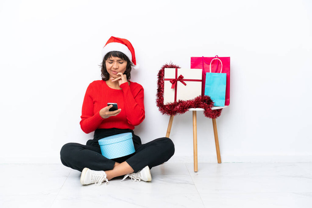 Junges Mädchen feiert Weihnachten auf dem Fußboden sitzend isoliert auf weißem Backgrund und sendet eine Botschaft - Foto, Bild