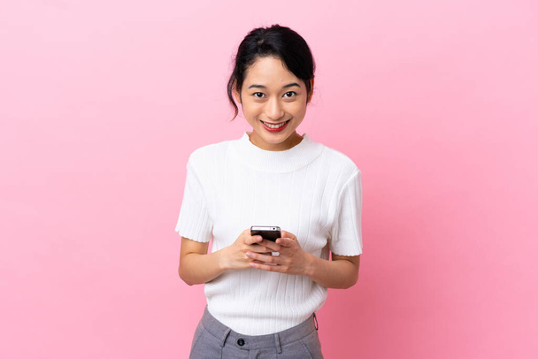 Jovem vietnamita isolada em fundo rosa enviando uma mensagem com o celular - Foto, Imagem