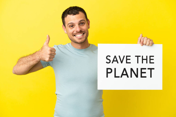 Brazilian man over isolated purple background holding a placard with text Save the Planet with thumb up - Fotó, kép