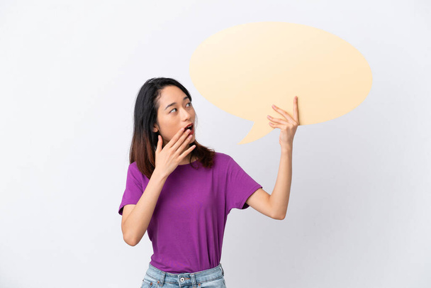Young Vietnamese woman isolated on white background holding an empty speech bubble with surprised expression - Фото, зображення