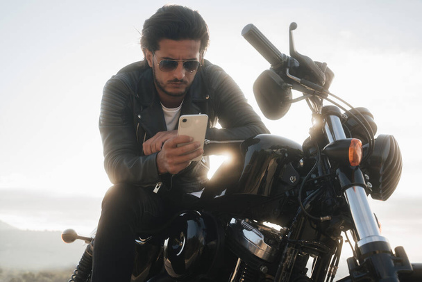 Handsome biker holding his smartphone, using navigation app to find the best road map - 写真・画像