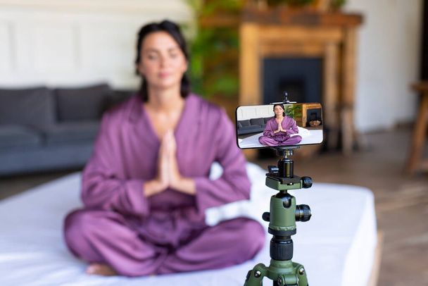 Une femme entraîneuse de yoga mène une leçon en ligne - la pratique de la méditation. Diffusion en ligne via smartphone. - Photo, image