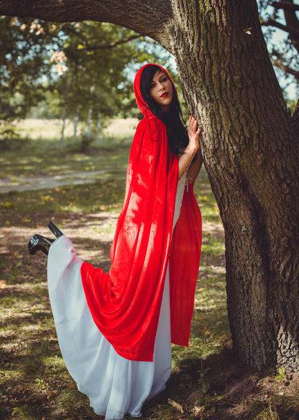 Halloween käsite, hohdokas puku yksityiskohta. Nuori kaunis ja salaperäinen nainen metsässä, valkoinen mekko ja punainen viitta. Pieni punainen huppu tai vampyyri tarina - Valokuva, kuva