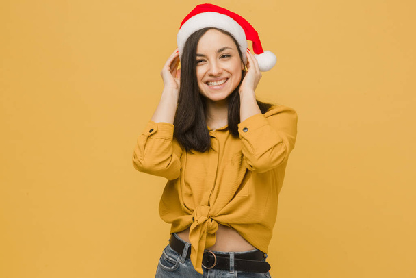 Photo of cute female in Christmas hat. Wears yellow shirt, isolated yellow color background - Photo, image