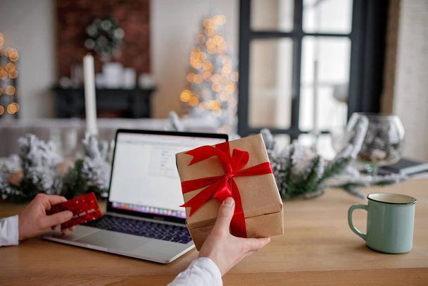 Adult man holds a gift for advent holiday on a laptop background. Makes online purchases. Happy New Year and Merry Christmas - Foto, Imagem