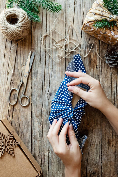 Ноль траты рождественских праздников. Руки держат стильный подарок, завернутый в хлопчатобумажную ткань на деревенском деревянном фоне с еловыми ветвями. Безпластичный устойчивый образ жизни - Фото, изображение