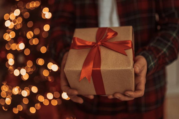 Dorosły mężczyzna trzyma w ręku pudełko z prezentem na adwentowe wakacje. Szczęśliwego Nowego Roku i Wesołych Świąt - Zdjęcie, obraz
