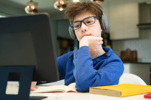 Online onderwijs op afstand. Een schooljongen studeert thuis en doet huiswerk op school. Een afstandsonderwijs thuis. - Foto, afbeelding