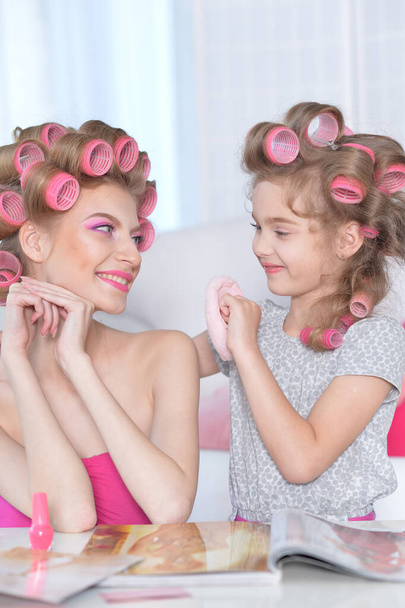 portrait of happy  mother and little daughter with hair curlers at home reading magazine - Φωτογραφία, εικόνα