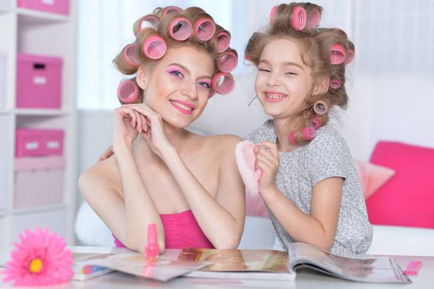 portrait of happy  mother and little daughter with hair curlers at home reading magazine - Fotoğraf, Görsel