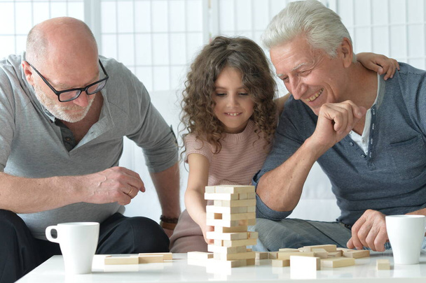 two senior men  sitting at table and playing with wooden blocks with granddaughter  - Photo, image
