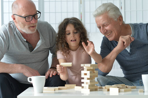 two senior men  sitting at table and playing with wooden blocks with granddaughter  - Fotografie, Obrázek