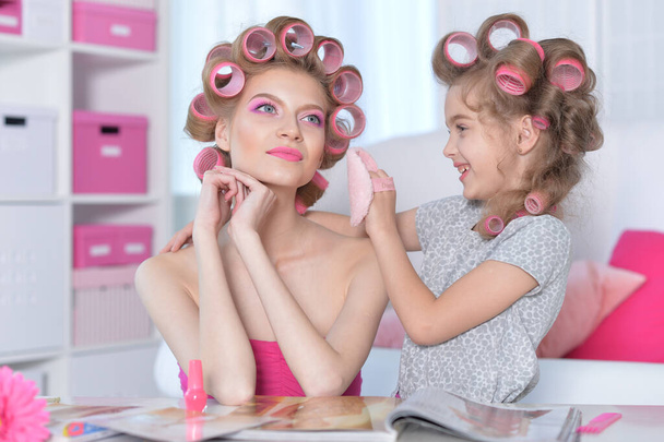 portrait of happy  mother and little daughter with hair curlers at home reading magazine - Foto, Imagem