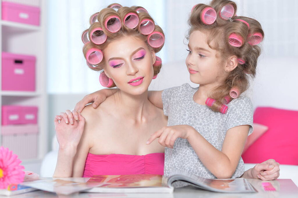  mother and little daughter with hair curlers reading magazine  - Foto, immagini