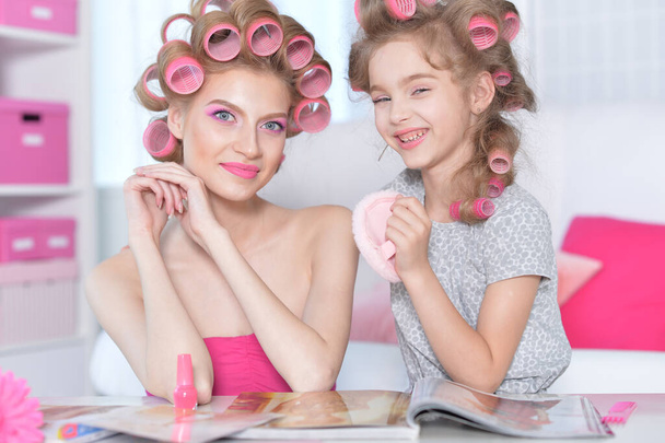 portrait of happy  mother and little daughter with hair curlers at home reading magazine - Foto, imagen