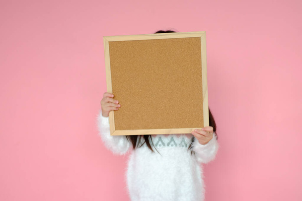 Portrait beautiful cute asian child girl on pink background with cork board texture holding in hand - Photo, Image