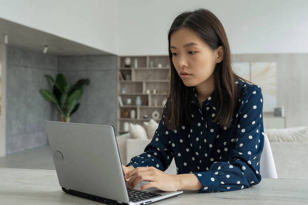 Asian business woman entrepreneur in a dark shirt and glasses, using a computer, looking at a screen, working at an office desk, smiling Asian professional woman typing e-mail on a laptop in the - 写真・画像