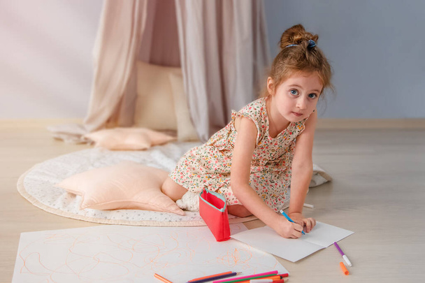 Ein kleines Mädchen zeichnet im Raum auf dem Fußboden. Die Sonnenstrahlen erhellen den Raum vom Fenster aus. - Foto, Bild