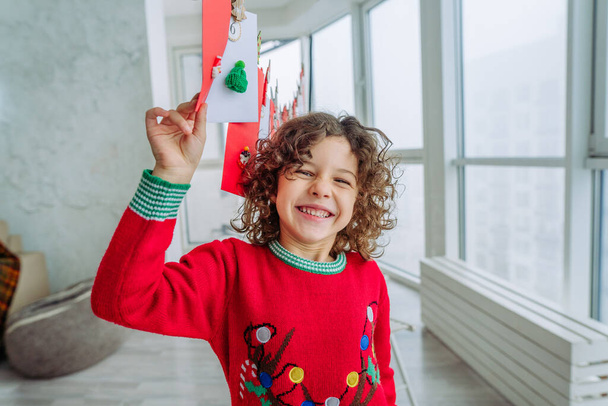Щасливий маленький хлопчик з кучерявим волоссям відкриває різдвяний календар пригод ручної роботи вдома
. - Фото, зображення