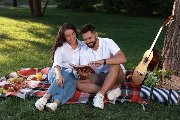 Glückliches junges Paar liest Buch auf Plaid im Park. Sommerpicknick - Foto, Bild