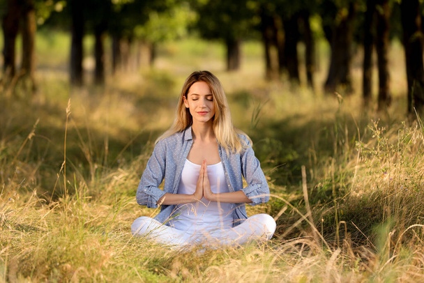 Young woman meditating in forest on sunny day - 写真・画像