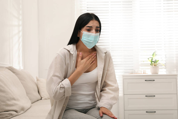 Young woman with protective mask suffering from breathing problem on sofa at home - Foto, Imagen