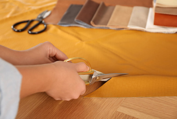 Woman cutting orange leather with scissors at wooden table, closeup - Foto, afbeelding