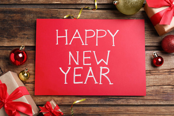 Feliz Año Nuevo tarjeta de felicitación. Papel rojo con frase y decoración sobre fondo de madera, plano - Foto, imagen
