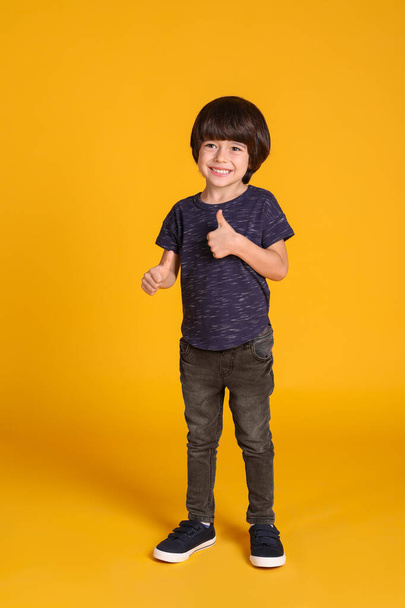 Full length portrait of cute little boy on yellow background - Photo, Image