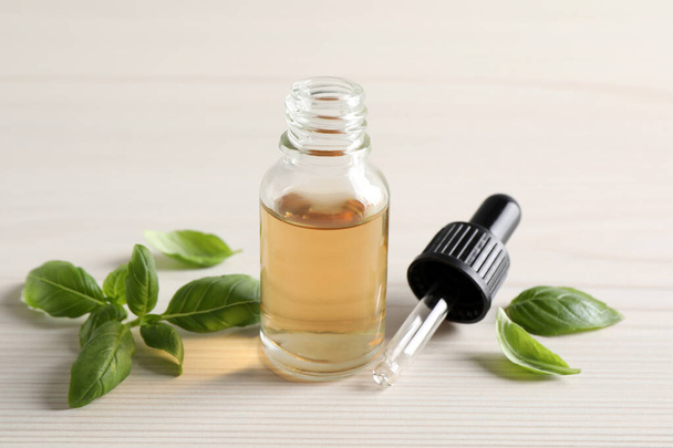 Glass bottle of basil essential oil and leaves on white  wooden table - Fotografie, Obrázek