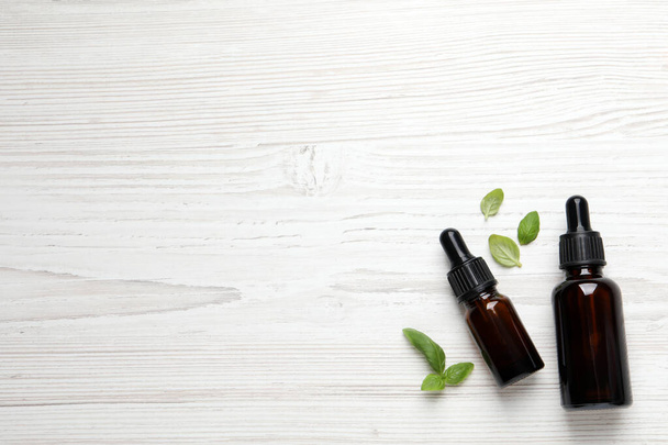 Glass bottles of basil essential oil and leaves on white  wooden table, flat lay. Space for text - Foto, immagini