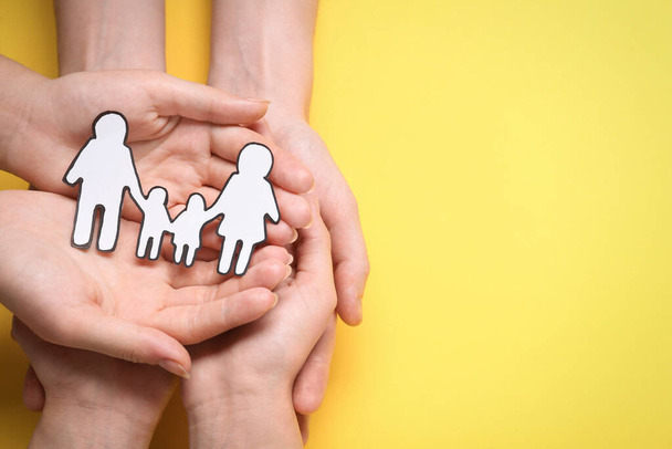 People holding paper family cutout on yellow background, top view. Space for text - Photo, image
