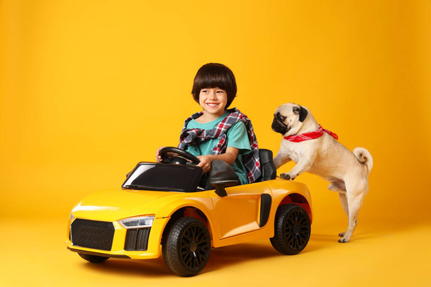 Little boy and his dog playing with toy car on yellow background - Fotó, kép