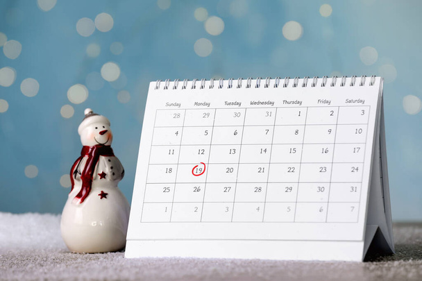 Saint Nicholas Day. Calendar with marked date December 19 and snowman figure on table against blurred lights - Photo, Image