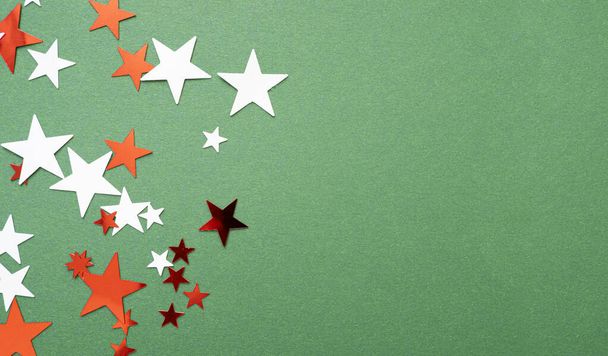 Christmas background with minimal composition, red and white stars on the top of green surface, flat lay, top view, space for text  - Foto, imagen