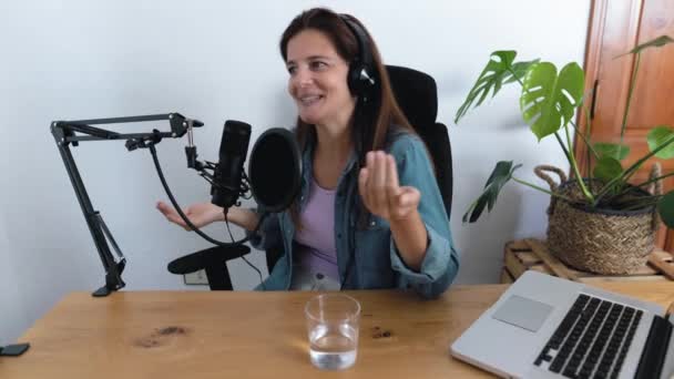 Mujer madura grabando un podcast usando micrófono y portátil desde su estudio en casa - Metraje, vídeo