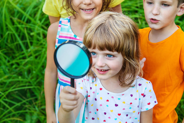 Children look at a magnifying glass on the nature. Selective focus. Nature. - Zdjęcie, obraz
