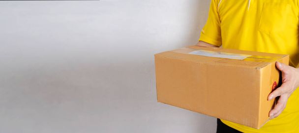 Delivery man in orange uniform handing a parcel box over to a customer, courier service concept - horizontal web banner background with copy space on the left - Foto, afbeelding