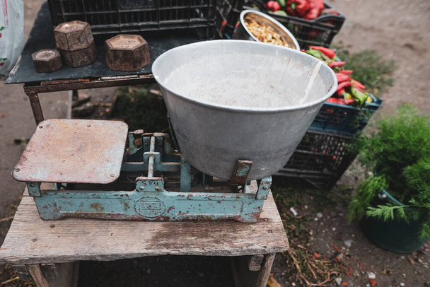 Ρηχό βάθος πεδίου (επιλεκτική εστίαση) εικόνα με βάρη παλαιάς κλίμακας στο τραπέζι ενός ρουμάνου αγρότη που πουλάει λαχανικά από τον κήπο του σε αγροτική περιοχή. - Φωτογραφία, εικόνα