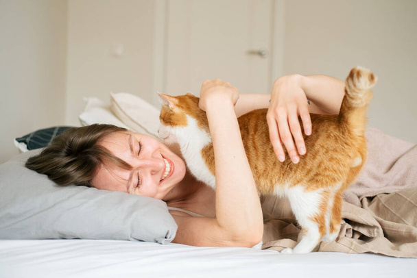 Portrait young beautiful caucasian woman wakes up in the morning. Woman hugging her cat at the morning. Lifestyle with home animals. - 写真・画像