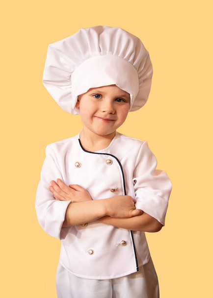 Uśmiechnięte dziecko w białym mundurze szefa kuchni. Wesoły żółty tło. - Zdjęcie, obraz