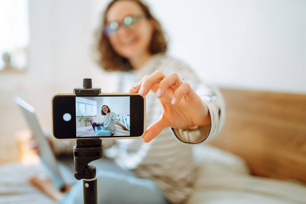 Video blog. Young woman looking into the camera and telling her story while leading a video blog. Vlogger makes online streaming using phone. Social media, instagram, stay home and quarantine. - Fotó, kép