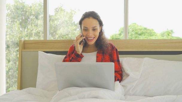 Sakin ol mutlu Latin iş kadını. Sosyal medya internetinde akıllı telefondan konuşan ve yatak odasındaki yatakta dizüstü bilgisayar teknolojisi kullanan insanlar. Yaşam biçimi - Fotoğraf, Görsel