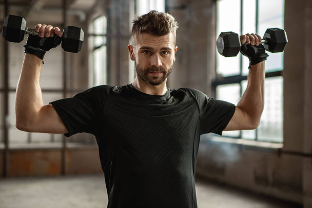 Strong sportsman working out with dumbbells in gym - Foto, imagen