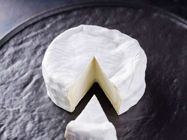 Camembert on a dark background. Soft cheese with white mold on a black plate. Minimalism. Copy space - Φωτογραφία, εικόνα
