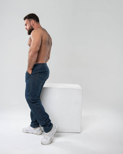 Мужчина без рубашки в синих джинсах на белом фоне в студии - Фото, изображение