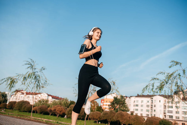 A girl in headphones is engaged in outdoor fitness in a metropolis. running and sports in summer - Fotó, kép