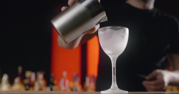 Бармен наливает смешанный напиток из шейкера в замороженное стекло с высоким стеблем, бармен делает коктейль со льдом и смешанным спиртом, 4k 120 кадров / с Прорес HQ - Кадры, видео