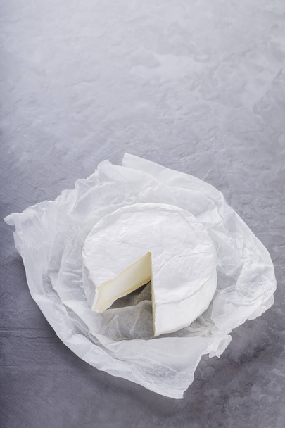 Camembert auf grauem Zementhintergrund. Weichkäse mit weißem Schimmel auf Pergamentpapier. Kopierraum. Ansicht von oben - Foto, Bild